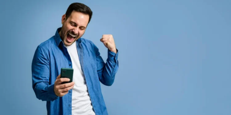 Homem comemorando e olhando para celular após ganhar na loteria