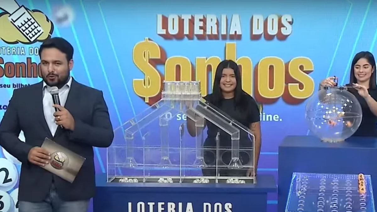 Apresentador anuncia os números da Loteria dos Sonhos de sexta-feira (14/03), com assistentes ao fundo realizando o sorteio