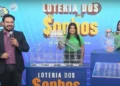 Apresentadores do sorteio da Loteria dos Sonhos com o globo e o caixa de números ao fundo