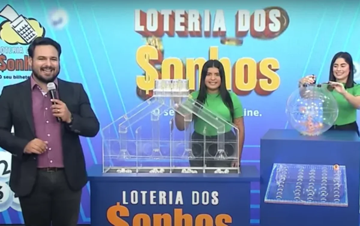 Apresentadores do sorteio da Loteria dos Sonhos, com um globo de números e uma casa transparente