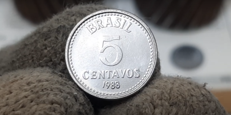 Moeda brasileira de 5 centavos do ano de 1988 segurada com luva