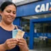 Mulher segura notas de dinheiro em frente à Caixa, representando os pagamentos do Bolsa Família de agosto realizados nesta semana.