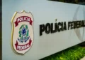 Placa da Polícia Federal do Brasil em destaque em uma estrutura metálica com fundo desfocado.