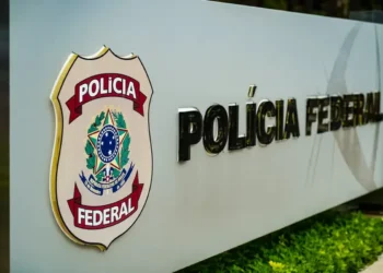 Placa da Polícia Federal do Brasil em destaque em uma estrutura metálica com fundo desfocado.