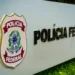 Placa da Polícia Federal do Brasil em destaque em uma estrutura metálica com fundo desfocado.