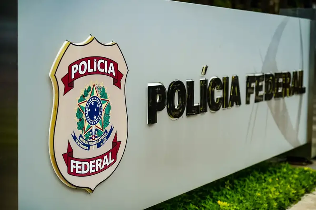 Placa da Polícia Federal do Brasil em destaque em uma estrutura metálica com fundo desfocado.