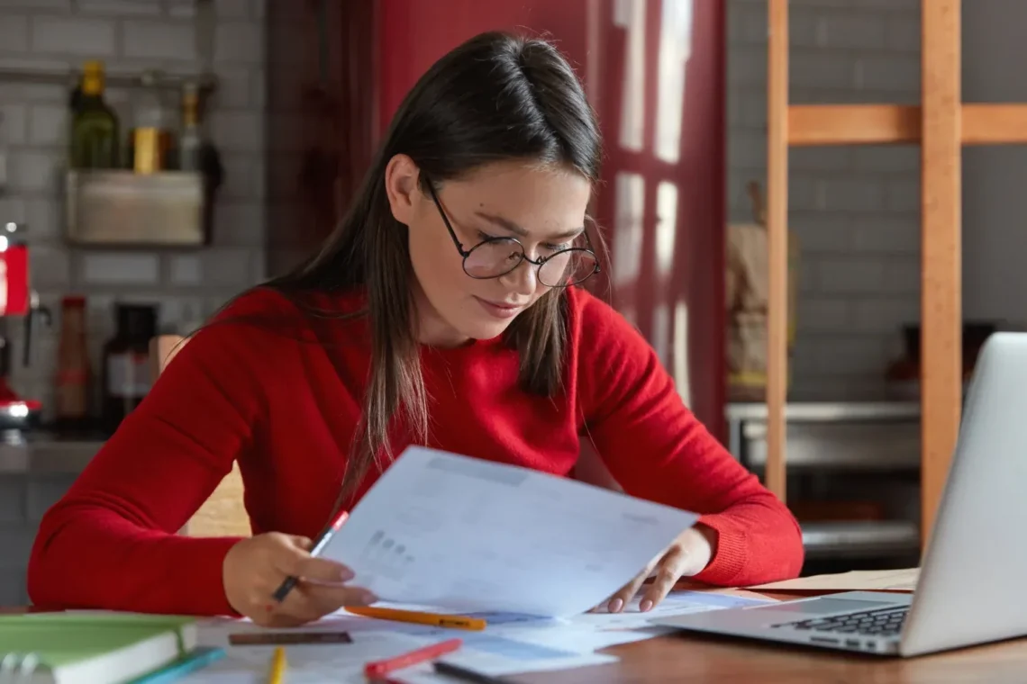 Mulher estudando concentrada para o concurso do INSS 2025, revisando documentos e fazendo anotações