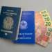 Passaporte, carteira de trabalho e cédulas de dinheiro em uma superfície cinza.