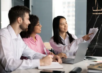 Equipe de trabalho colaborando em uma reunião, analisando documentos e discutindo ideias em um ambiente corporativo moderno