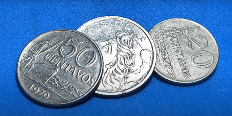 Três moedas brasileiras de 1970, incluindo as de 20 e 50 centavos, sobre fundo azul