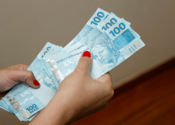 Pessoa segurando cédulas de R$ 100 em mãos.