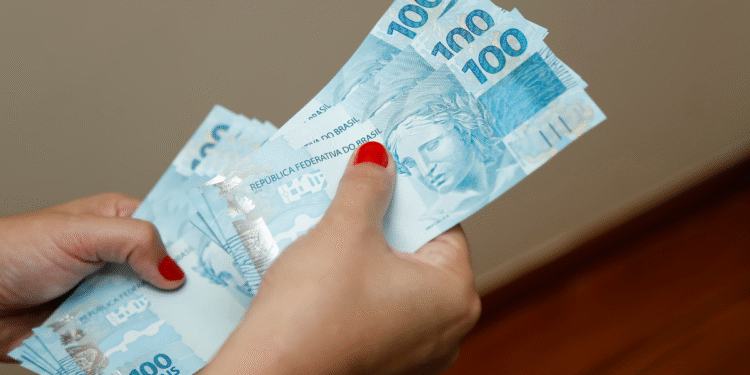 Pessoa segurando cédulas de R$ 100 em mãos.