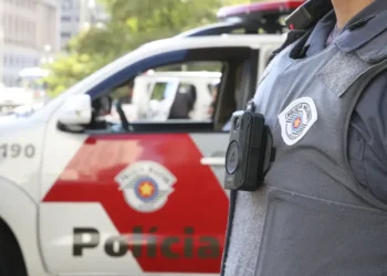 Policial militar em uniforme, com carro de patrulha ao fundo, simbolizando o concurso da PM-TO.