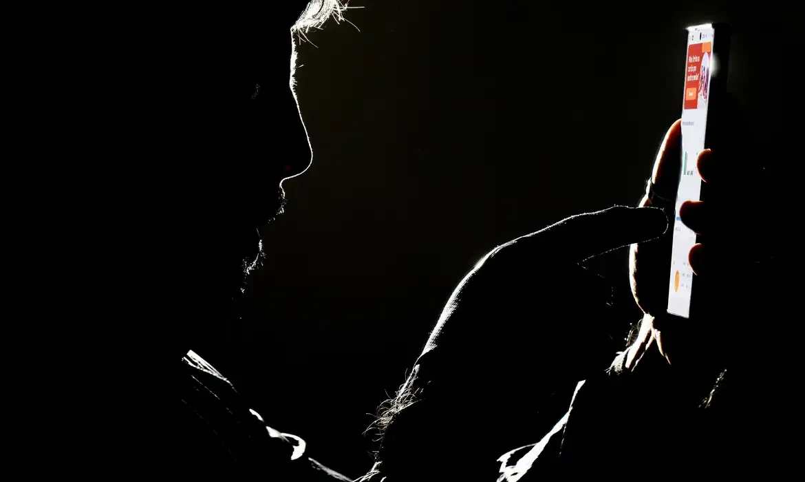 Manipulação de celular em ambiente escuro Silhueta de uma pessoa manipulando um smartphone em um ambiente escuro.