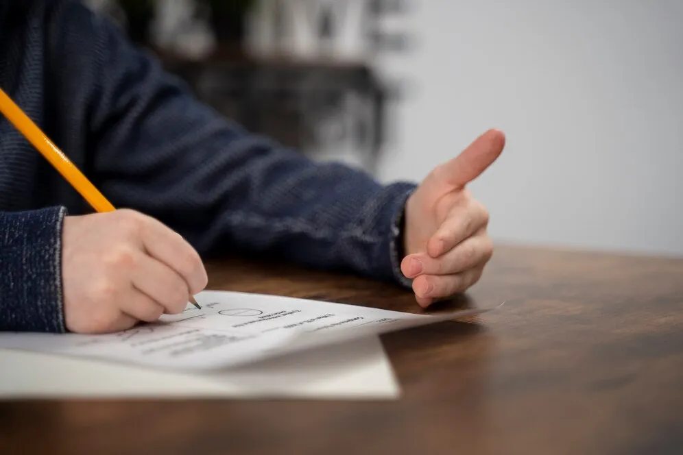 Mão segurando um lápis enquanto preenche um formulário de inscrição, representando as inscrições online do concurso PM-PR