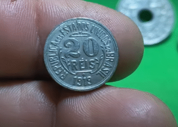 moeda de 20 réis de 1918 sendo segurada por uma mão em fundo verde