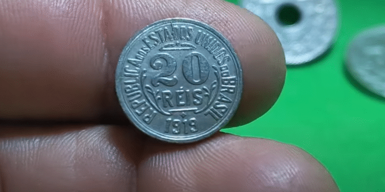 moeda de 20 réis de 1918 sendo segurada por uma mão em fundo verde