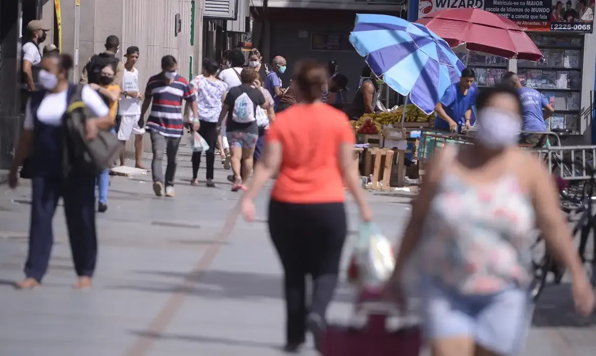 Pessoas andando nas ruas de São Paulo Pessoas caminhando em uma rua com máscaras, no centro da cidade, com barracas de frutas ao fundo.