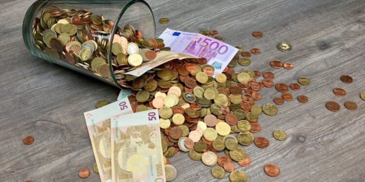 Moedas de ouro e prata das Olimpíadas, com notas de 50 e 500 euros espalhadas em um chão de madeira.