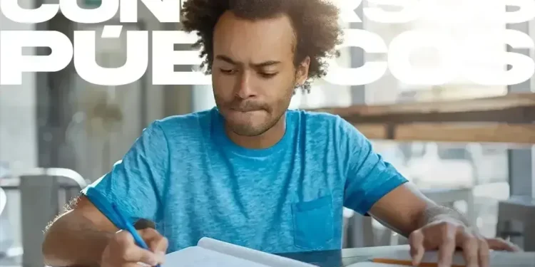 Homem de camiseta azul escrevendo em um caderno, com uma expressão concentrada, indicando a preparação para o concurso