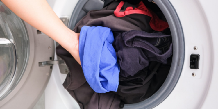 Pessoa colocando roupas coloridas na máquina de lavar, simbolizando economia de energia ao escolher horários mais baratos.