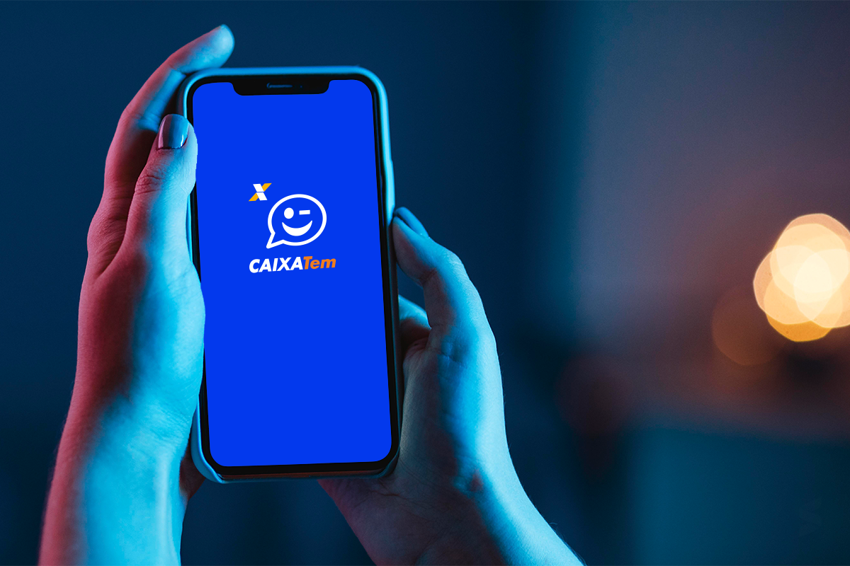 Como consultar o pagamento Pessoa segurando celular com tela do aplicativo Caixa Tem, em ambiente escuro.