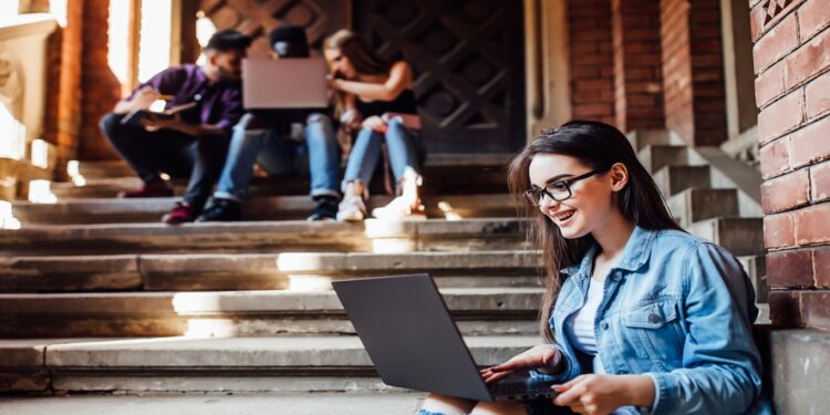 Estudantes universitários sentados em escadas de uma universidade usando notebooks e estudando juntos.