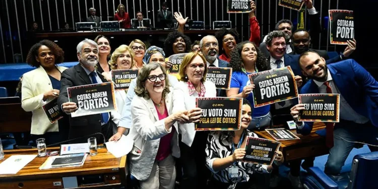 Grupo de senadores celebrando a aprovação da Lei de Cotas no Senado, com cartazes dizendo 'Eu voto sim pela Lei de Cotas'.