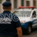 Policial da Guarda Municipal com carro de patrulha ao fundo, destacando o concurso aberto.