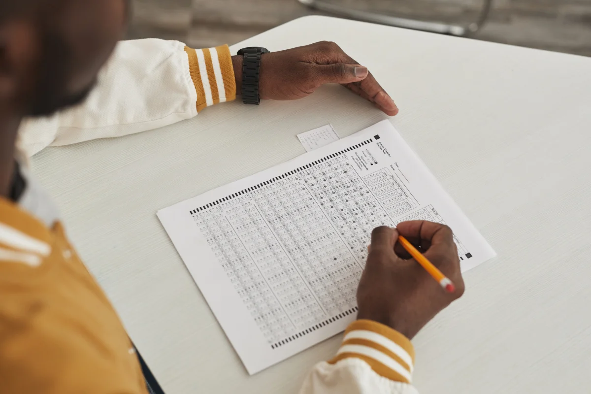 Preenchendo Ficha de Inscrição para Concurso Pessoa preenchendo a ficha de inscrição de concurso, com um lápis na mão e olhando atentamente.