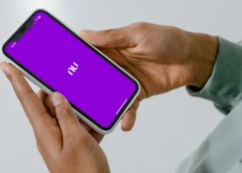 Mãos segurando smartphone com tela roxa do aplicativo Nubank aberto.
