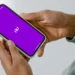 Mãos segurando smartphone com tela roxa do aplicativo Nubank aberto.