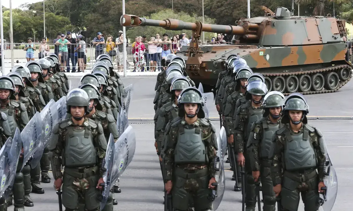 Soldados do Exército Brasileiro marchando durante uma apresentação militar com um tanque ao fundo.