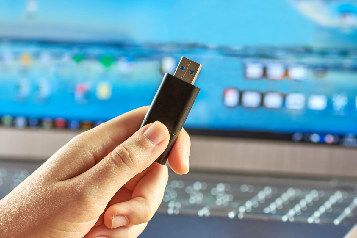 Aprenda novas funcionalidades para seu bom e velho pendrive Pessoa segurando um pendrive em frente do computador.