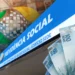 Fachada do prédio da Previdência Social com diversas cédulas de reais, representando a devolução dos descontos indevidos pelo INSS.