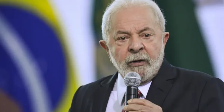 Ex-presidente Lula falando ao microfone durante evento oficial com bandeira do Brasil ao fundo.