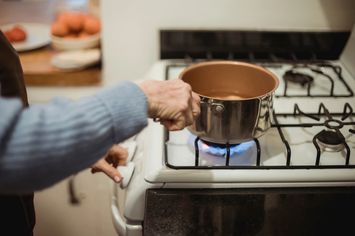  Pessoa ajustando o fogo do fogão a gás enquanto segura uma panela de metal.