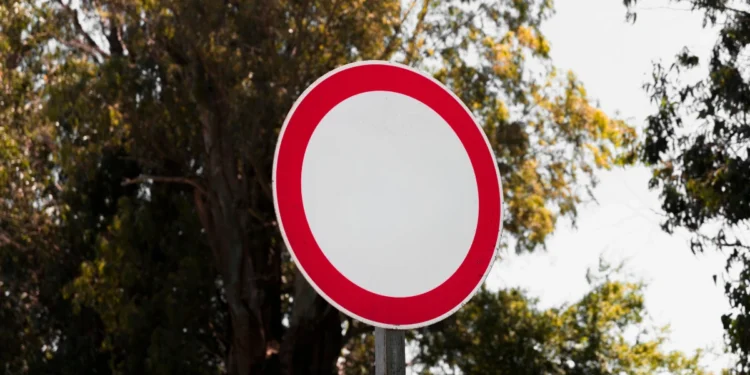 Placa de trânsito circular com borda vermelha em área arborizada