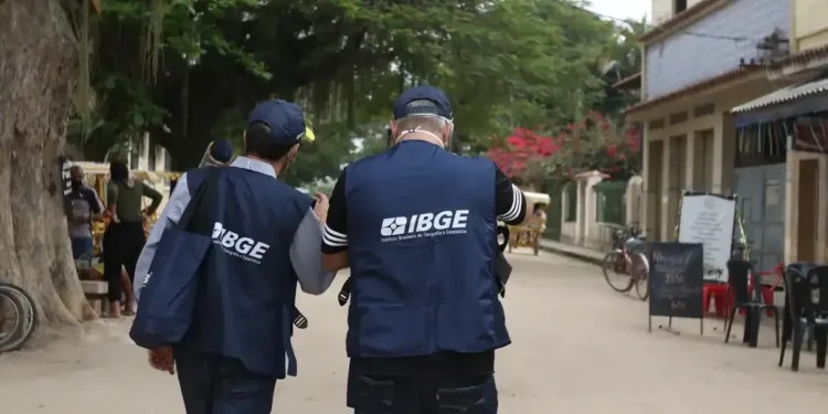 Dois agentes do IBGE caminham por rua arborizada durante coleta de dados em comunidade.