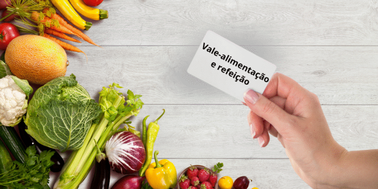 Mão segurando cartão de vale-alimentação com legumes frescos ao fundo