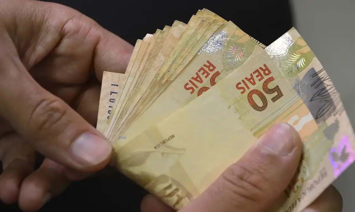 bolsa família Cédulas de dinheiro brasileiro em mãos simbolizando o valor do Bolsa Família