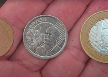 Três moedas brasileiras raras sendo exibidas na palma da mão: 5 centavos, 1 real e comemorativa