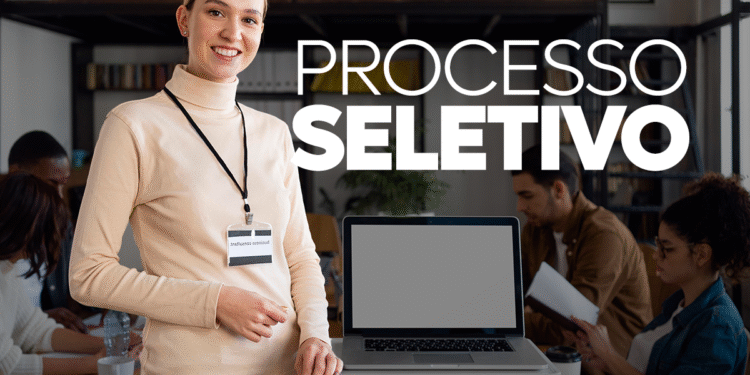 Mulher em reunião, sorrindo enquanto segura um crachá, com laptop e colegas ao fundo.