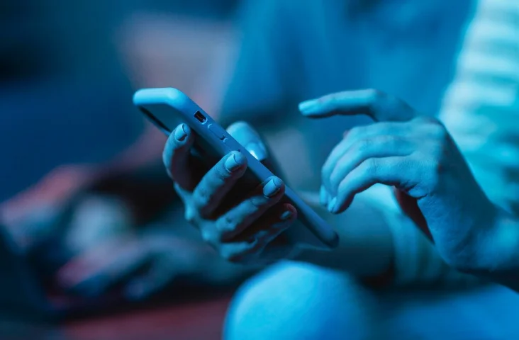 Controle total do plano direto no app Pessoa segurando o celular e acessando aplicativo com iluminação azul