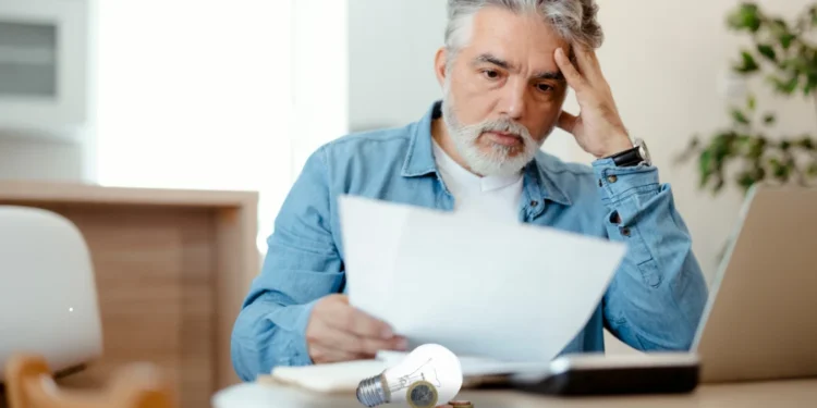 Homem preocupado com aumento de tarifa de energia ao verificar conta de luz.