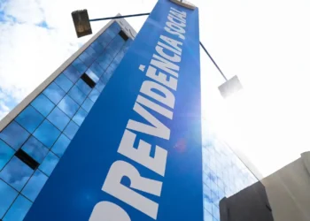 Edifício moderno com fachada espelhada sob céu azul e placa azul da Previdência Social