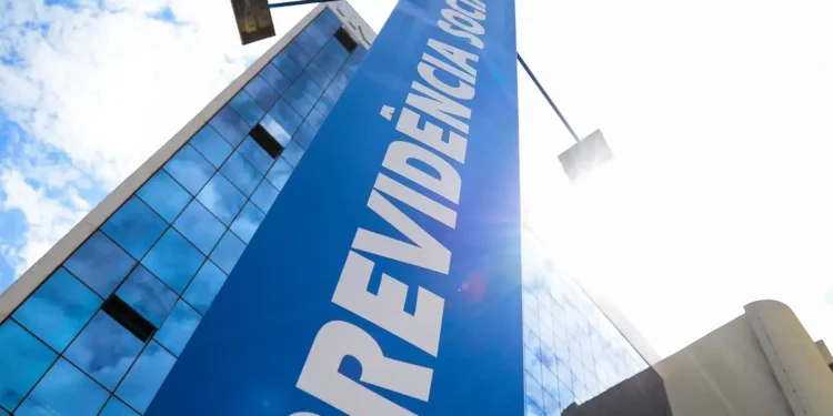 Edifício moderno com fachada espelhada sob céu azul e placa azul da Previdência Social