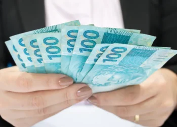 Pessoa segura várias cédulas de 100 reais nas mãos.