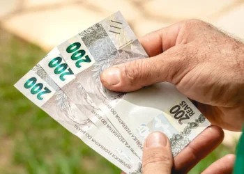 Mãos segurando cédulas de 200 reais representando pagamento de benefícios sociais