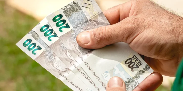 Mãos segurando cédulas de 200 reais representando pagamento de benefícios sociais